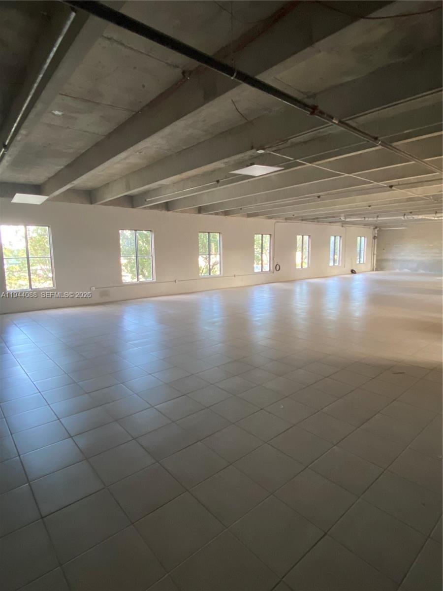 An empty, open-plan commercial space features tiled flooring, white walls, and exposed concrete ceilings — PALMETTO BAY, FL