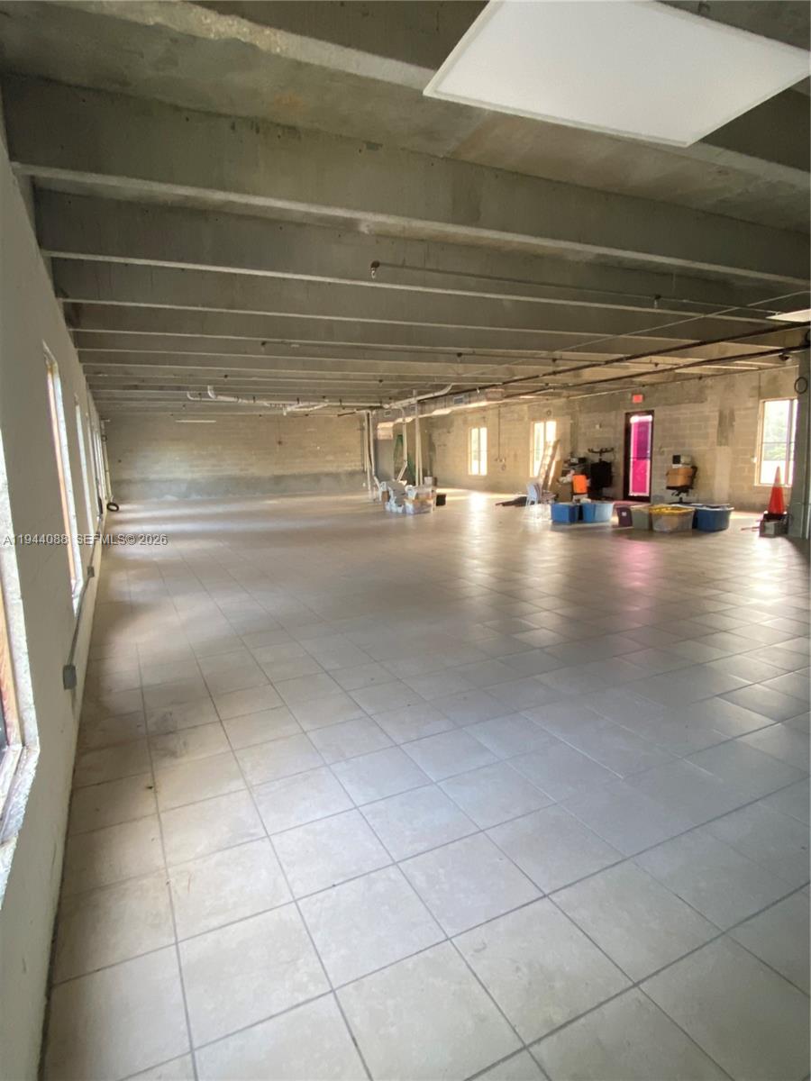 An open-plan commercial space features exposed concrete ceilings, tiled flooring, and multiple windows — PALMETTO BAY, FL