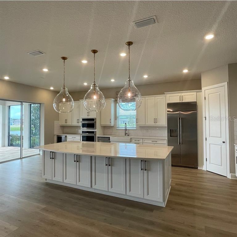 A kitchen features white cabinets, a large island with pendant lights, and stainless steel appliances — 4364 CURACAO PLACE, KISSIMMEE, FL