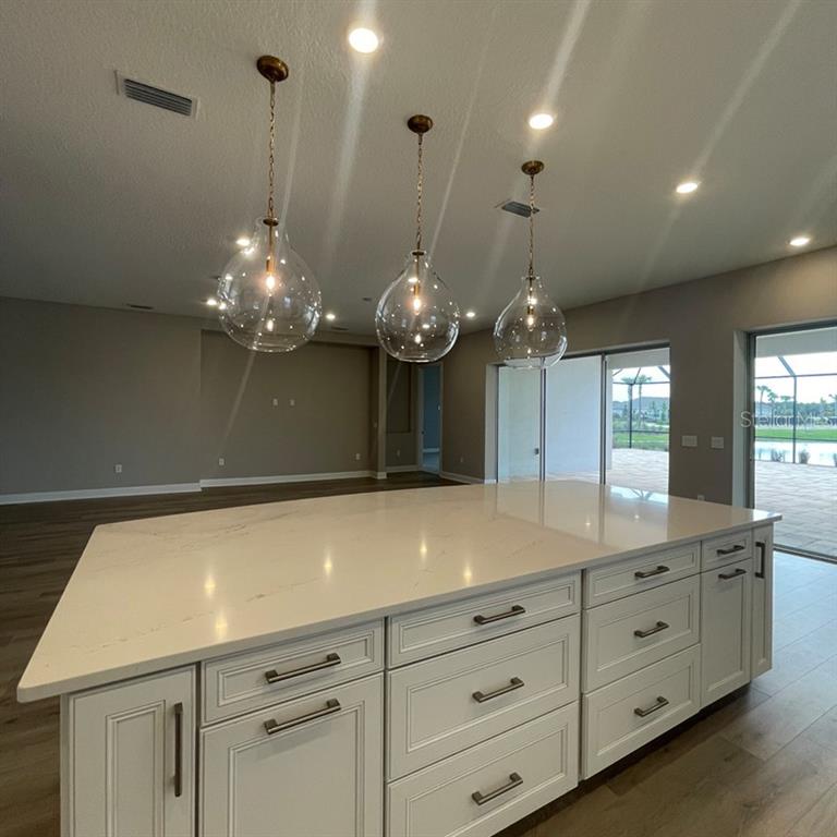 A kitchen island with white cabinets and a quartz countertop sits beneath three glass pendant lights — 4364 CURACAO PLACE, KISSIMMEE, FL