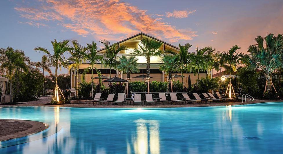 A swimming pool sits in front of a clubhouse building surrounded by palm trees at sunset — 4364 CURACAO PLACE, KISSIMMEE, FL