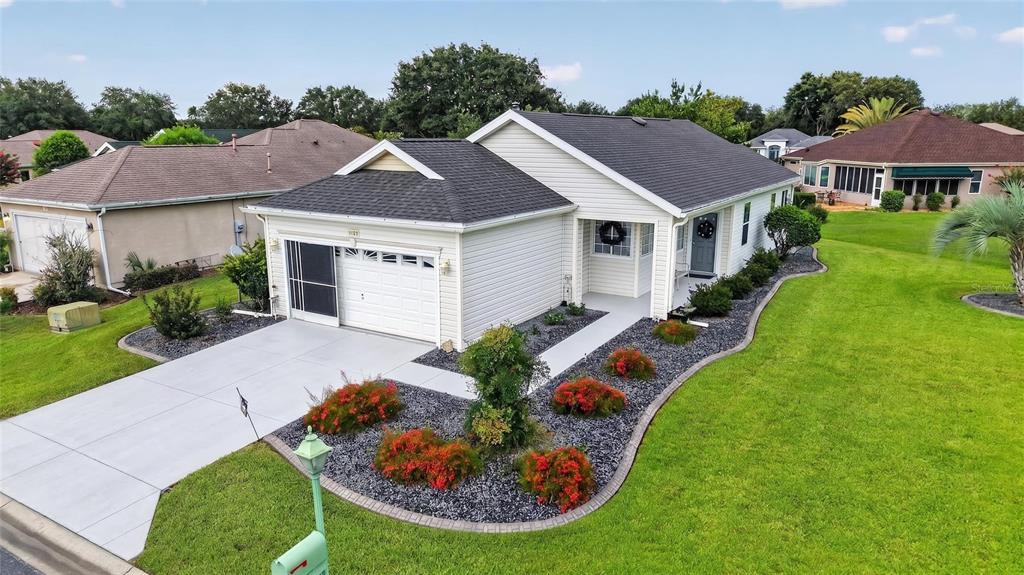 An exterior view of a single-story house with a white garage, gray roof, and landscaping — 12771 SE 92ND TERRACE, SUMMERFIELD, FL