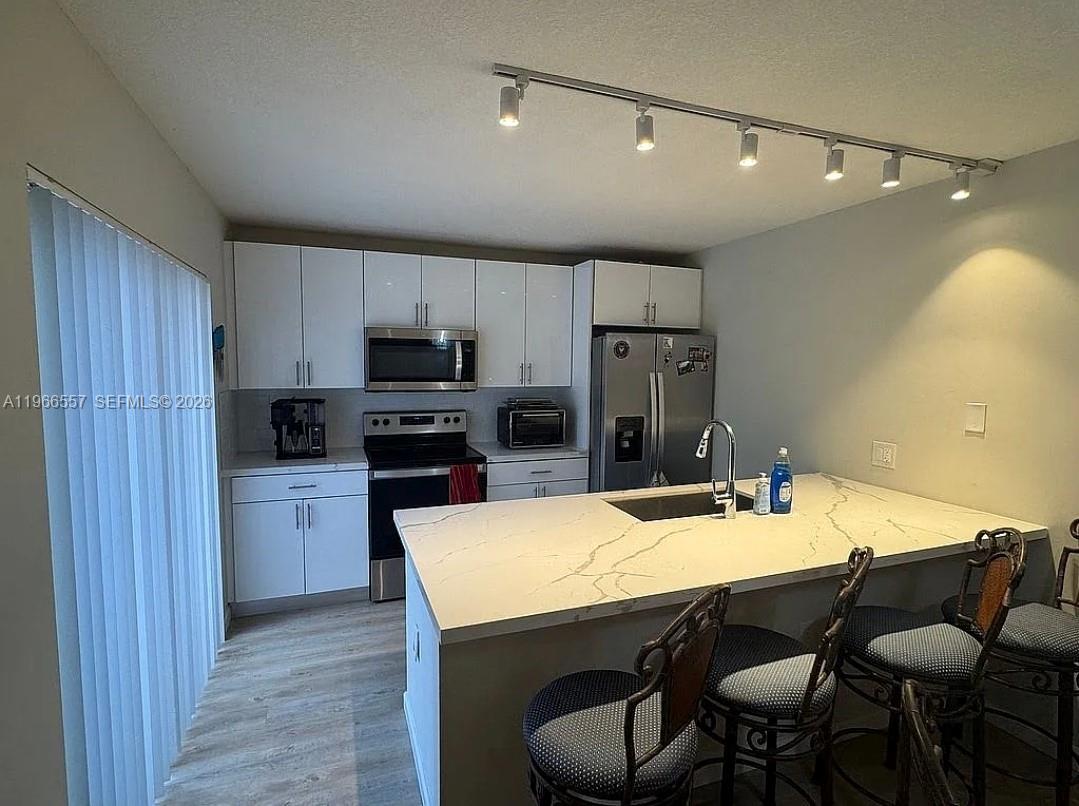 A modern kitchen features white cabinets, stainless steel appliances, and a large marble-topped island — 6222 62nd Way, West Palm Beach FL 33409, WEST PALM BEACH, FL