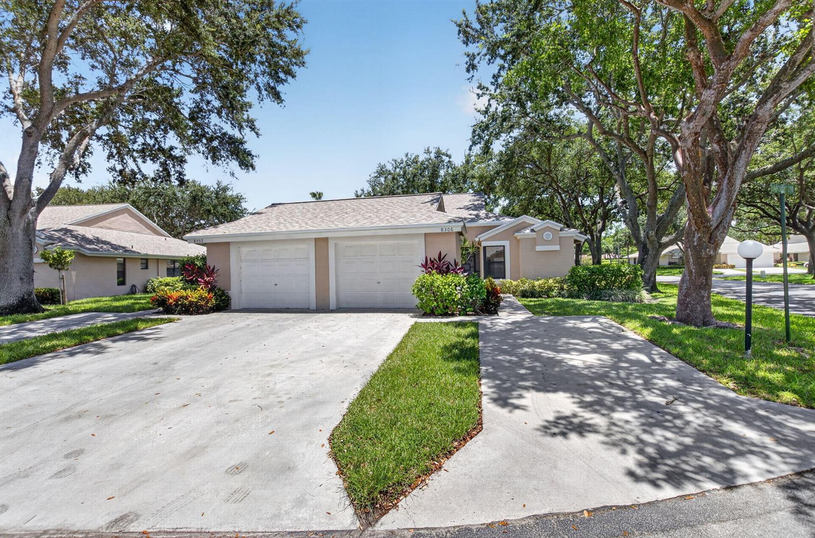 A single-story duplex with two garage doors, a concrete driveway, and surrounding mature trees — 8306 Summersong Terrace, Boca Raton FL 33496, BOCA RATON, FL