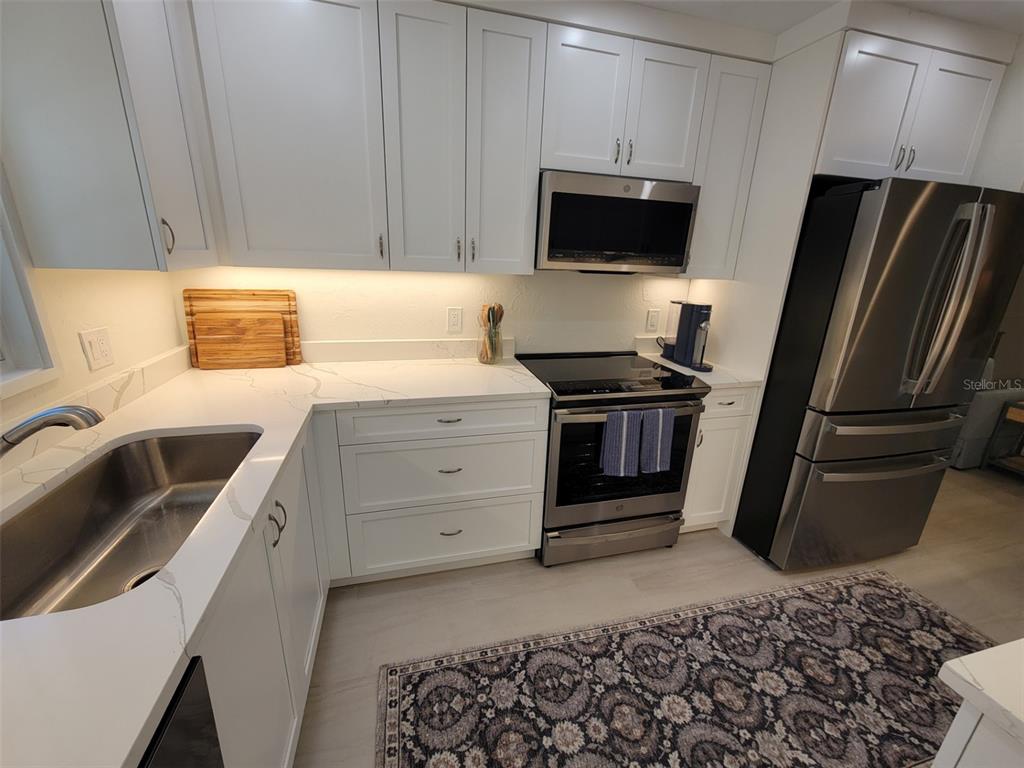 A modern kitchen features white cabinets, stainless steel appliances, and white marble-look countertops — 323 MADISON DRIVE, SARASOTA, FL
