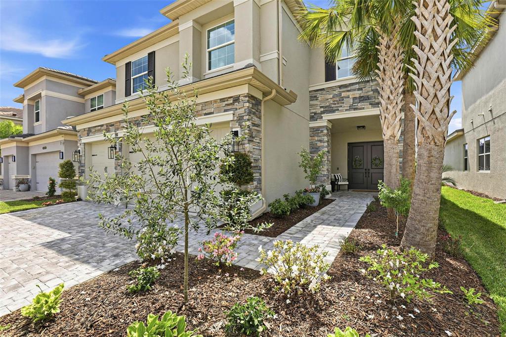 A two-story house with a stone facade, paved driveway, and palm trees in the front yard — 32490 TREE OF LIFE AVENUE, WESLEY CHAPEL, FL
