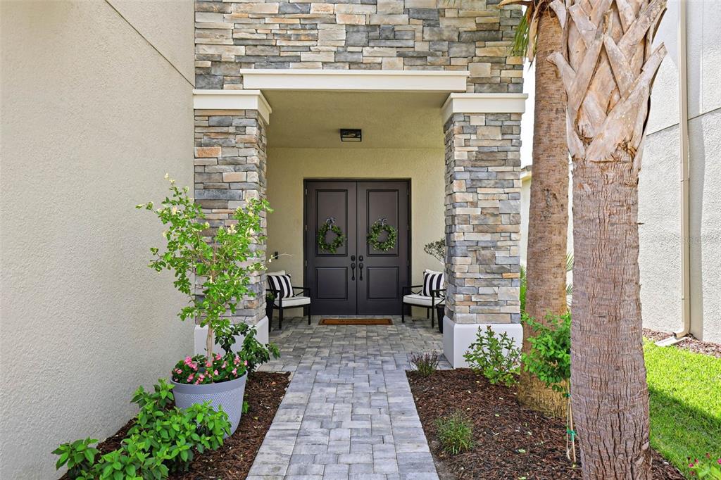 A stone-accented entryway features a paved walkway leading to double front doors with wreaths — 32490 TREE OF LIFE AVENUE, WESLEY CHAPEL, FL