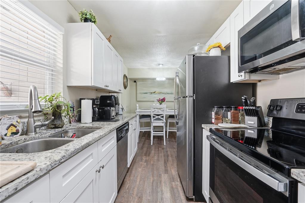 A galley kitchen features white cabinets, granite countertops, stainless steel appliances, and a dining area — 1410 KOZART COURT, ORLANDO, FL