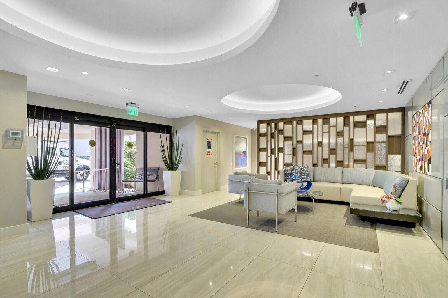 A modern lobby features a seating area with a sectional sofa, tile floors, and glass doors — 2697 N Ocean Boulevard # 604, Boca Raton FL 33431, BOCA RATON, FL