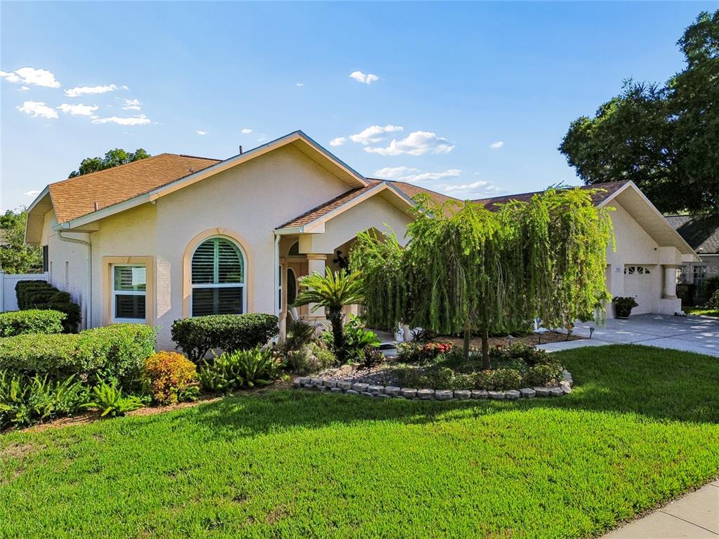 A single-story house with a tan exterior, a brown roof, and a landscaped front yard — 9002 TARAWYND CT, ODESSA, FL