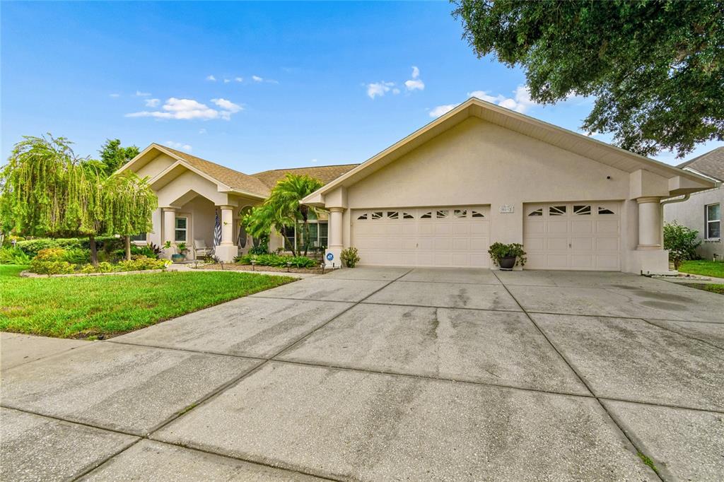A single-story house with a beige stucco exterior, a three-car garage, and a concrete driveway — 9002 TARAWYND CT, ODESSA, FL