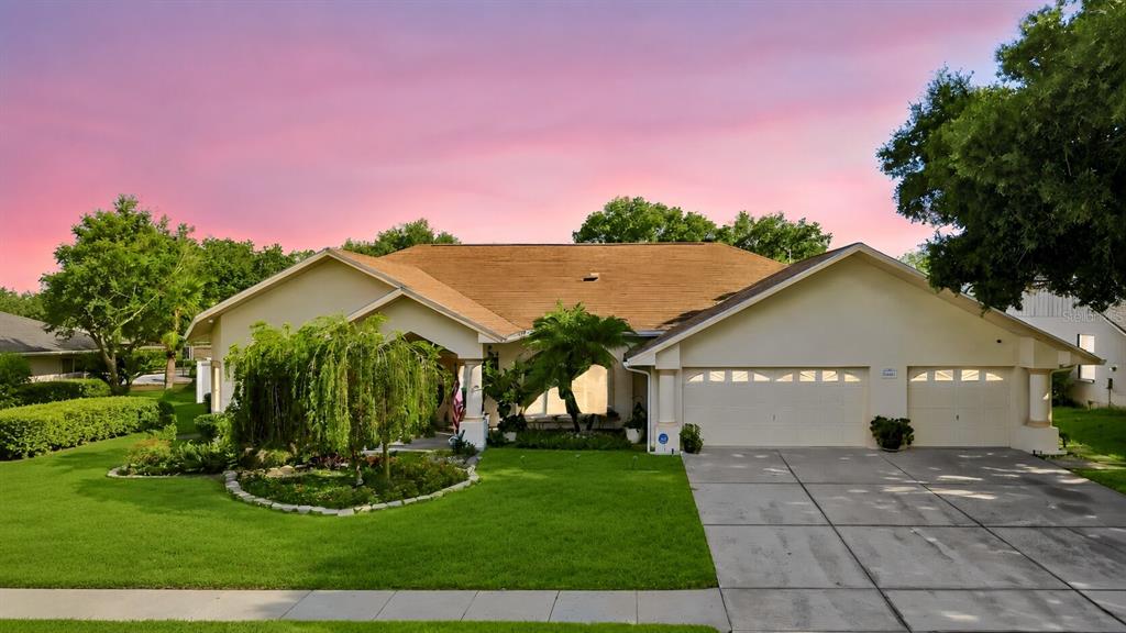 A single-story house with a tan roof, white exterior, and a two-car garage at sunset — 9002 TARAWYND CT, ODESSA, FL