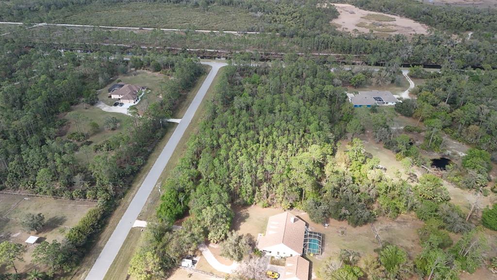 An aerial view shows a residential property with a pool, surrounded by dense wooded land — ESTATES DRIVE, NORTH PORT, FL