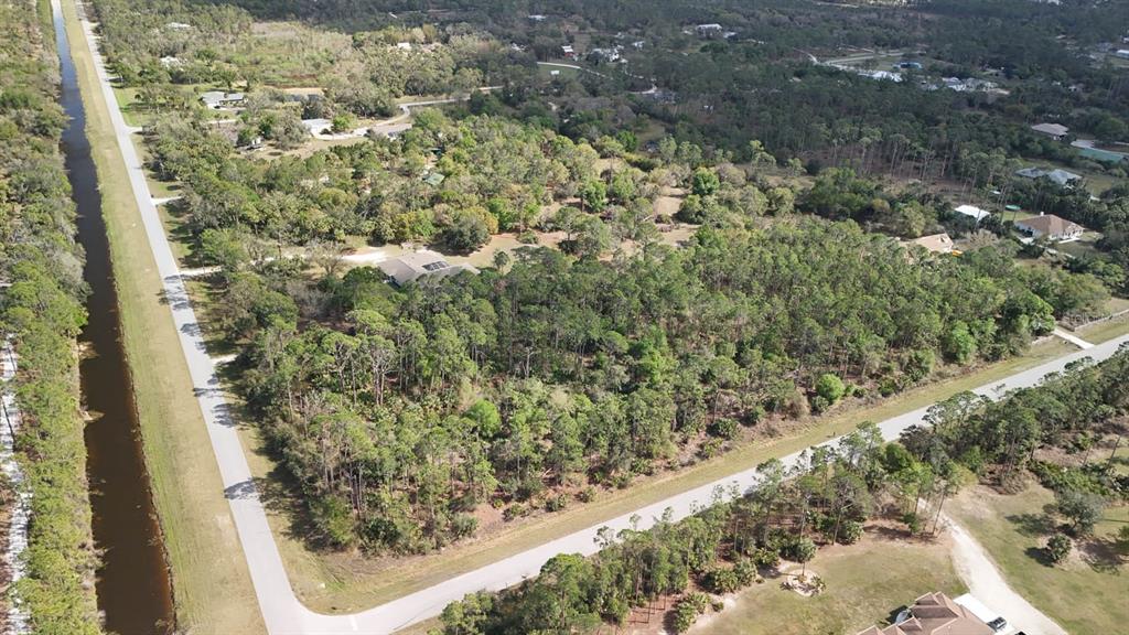 An aerial view shows a wooded residential lot bordered by a canal and paved roads — ESTATES DRIVE, NORTH PORT, FL