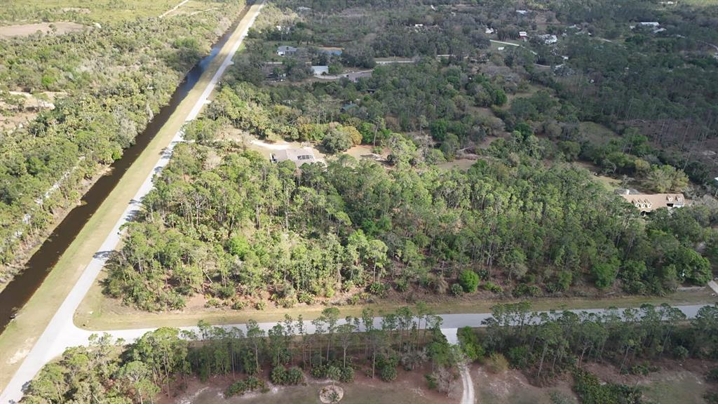 An aerial view shows a wooded lot bordered by a canal and paved roads — ESTATES DRIVE, NORTH PORT, FL