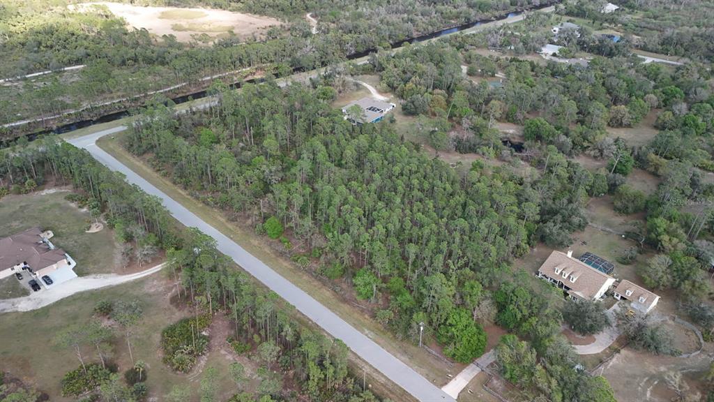 An aerial view shows a wooded lot situated between two houses along a paved road — ESTATES DRIVE, NORTH PORT, FL