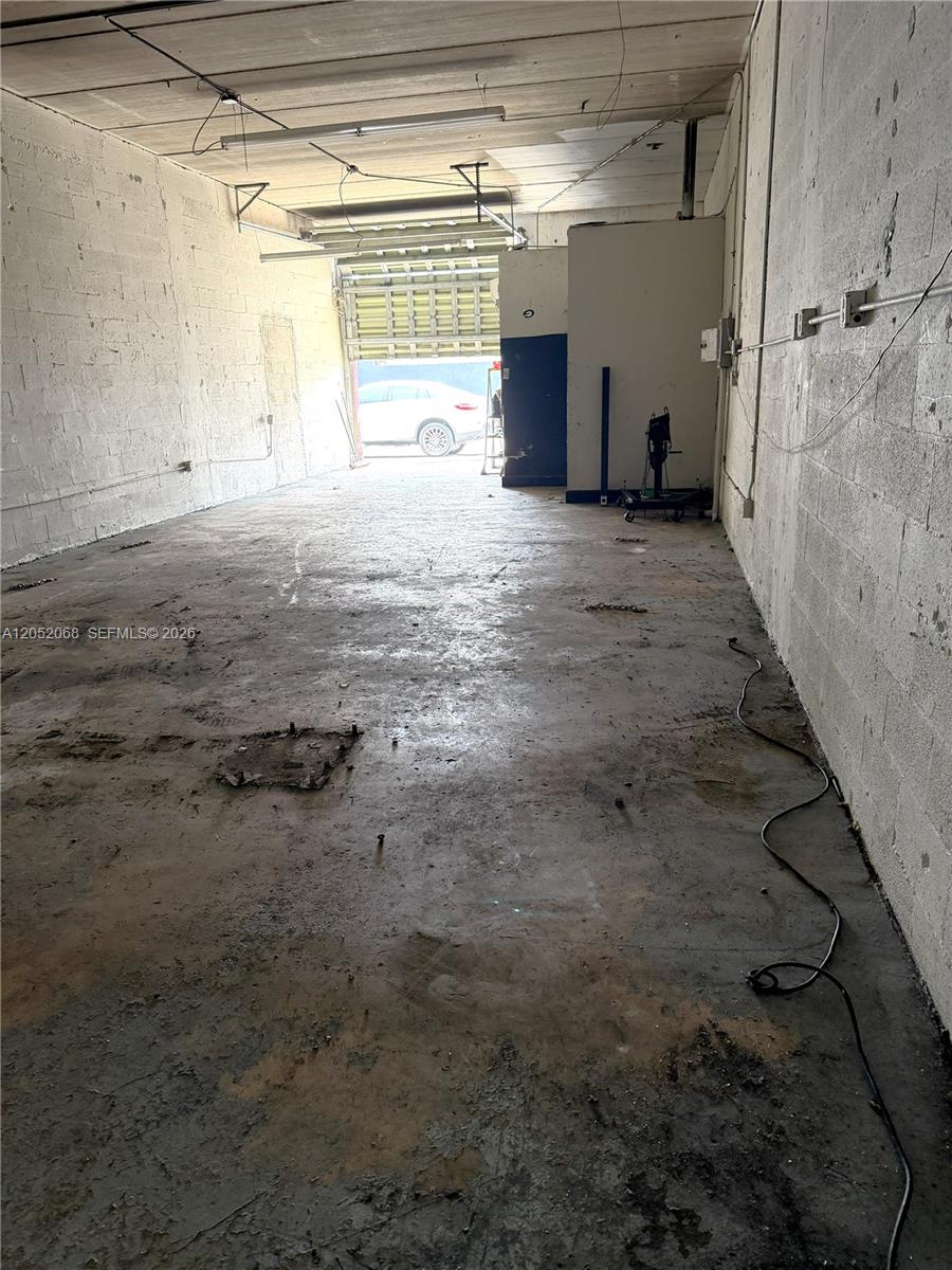 An empty industrial warehouse space features concrete block walls, a concrete floor, and a roll-up door — 2561 NW 23rd St, Miami FL 33142, MIAMI, FL