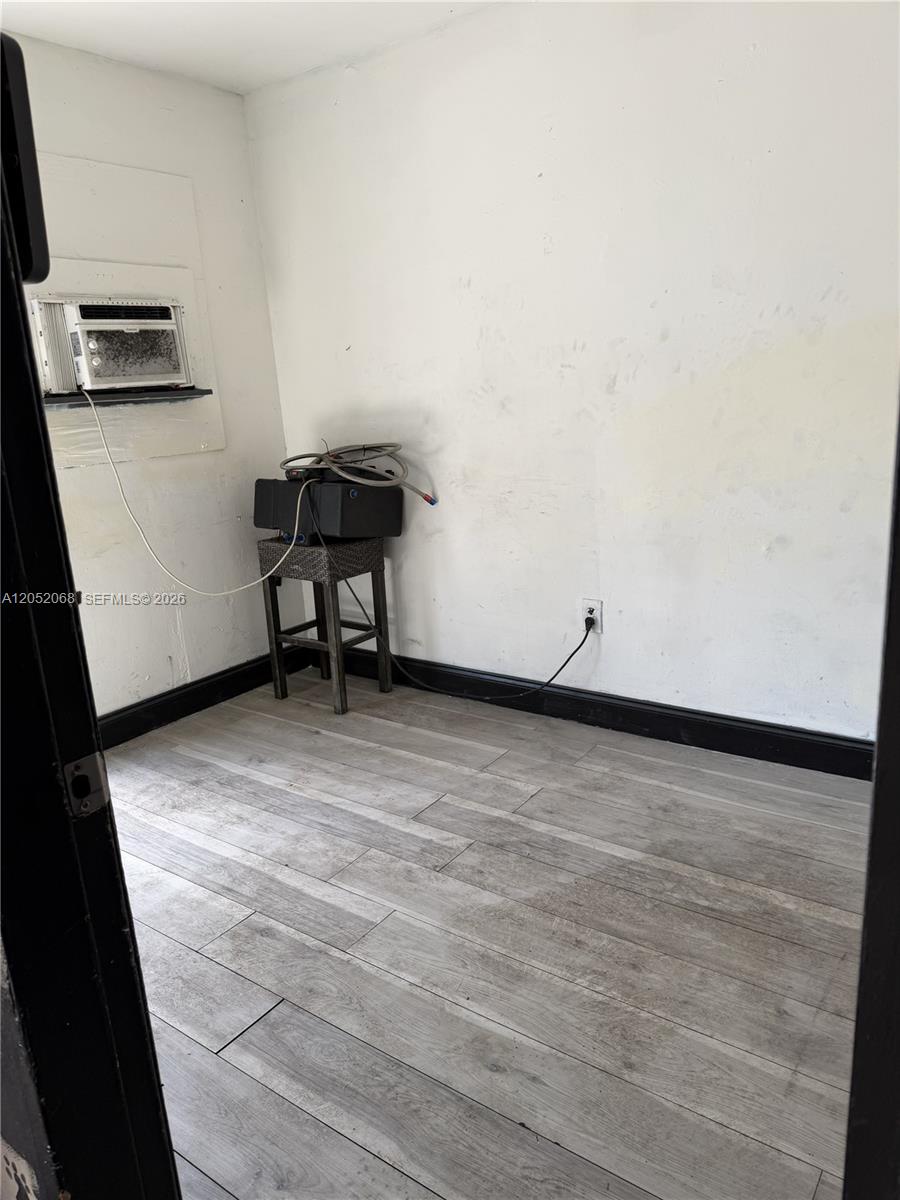 A small room features light wood-look flooring, white walls, a window air conditioner, and a stool — 2561 NW 23rd St, Miami FL 33142, MIAMI, FL