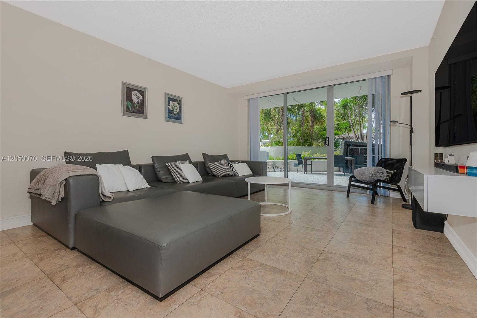 A living room features a grey sectional sofa, tile flooring, and sliding glass doors to a patio — 1500 Bay Rd # 116S, Miami Beach FL 33139, MIAMI BEACH, FL