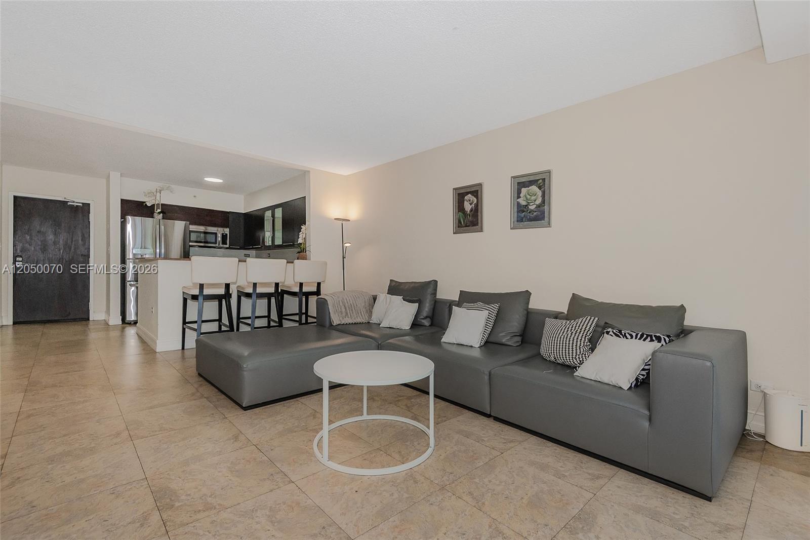 A living room features a grey sectional sofa, a white coffee table, and an open kitchen — 1500 Bay Rd # 116S, Miami Beach FL 33139, MIAMI BEACH, FL