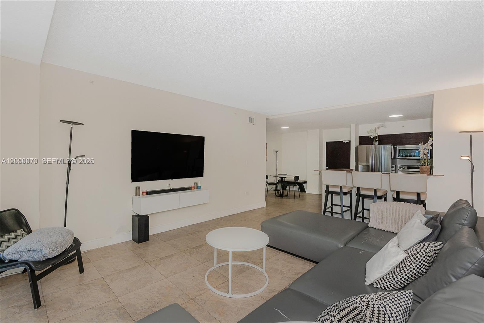 A living room with tile floors, a wall-mounted television, and an open kitchen area — 1500 Bay Rd # 116S, Miami Beach FL 33139, MIAMI BEACH, FL