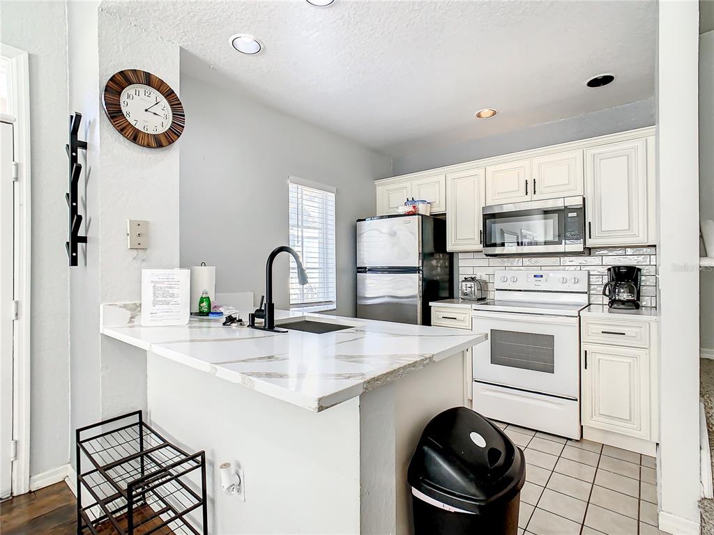A kitchen features white cabinets, stainless steel appliances, and a marble-topped island with a sink — 2211 SAN VITTORINO CIRCLE UNIT 102, KISSIMMEE, FL