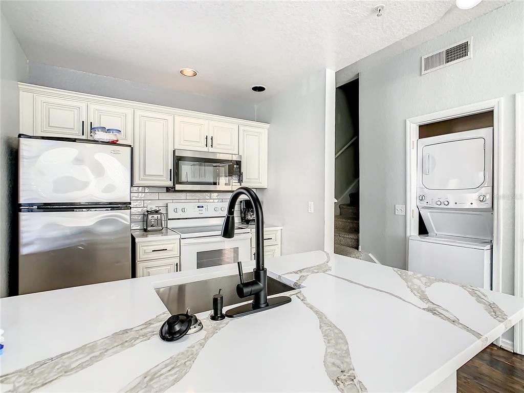 A kitchen features white cabinets, stainless steel appliances, a quartz island, and a stacked laundry unit — 2211 SAN VITTORINO CIRCLE UNIT 102, KISSIMMEE, FL