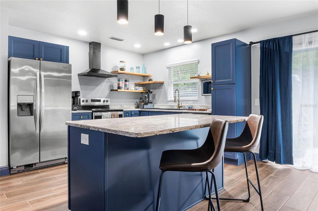A kitchen features blue cabinets, a granite-topped island, stainless steel appliances, and wood-look flooring — 3761 N HIAWATHA TER, CRYSTAL RIVER, FL