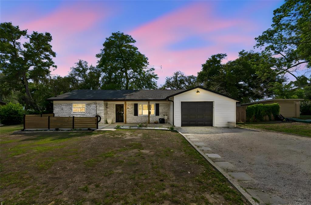 A single-story house with a white brick facade, dark garage door, and a gravel driveway — 118 HORST ROAD, BRANDON, FL