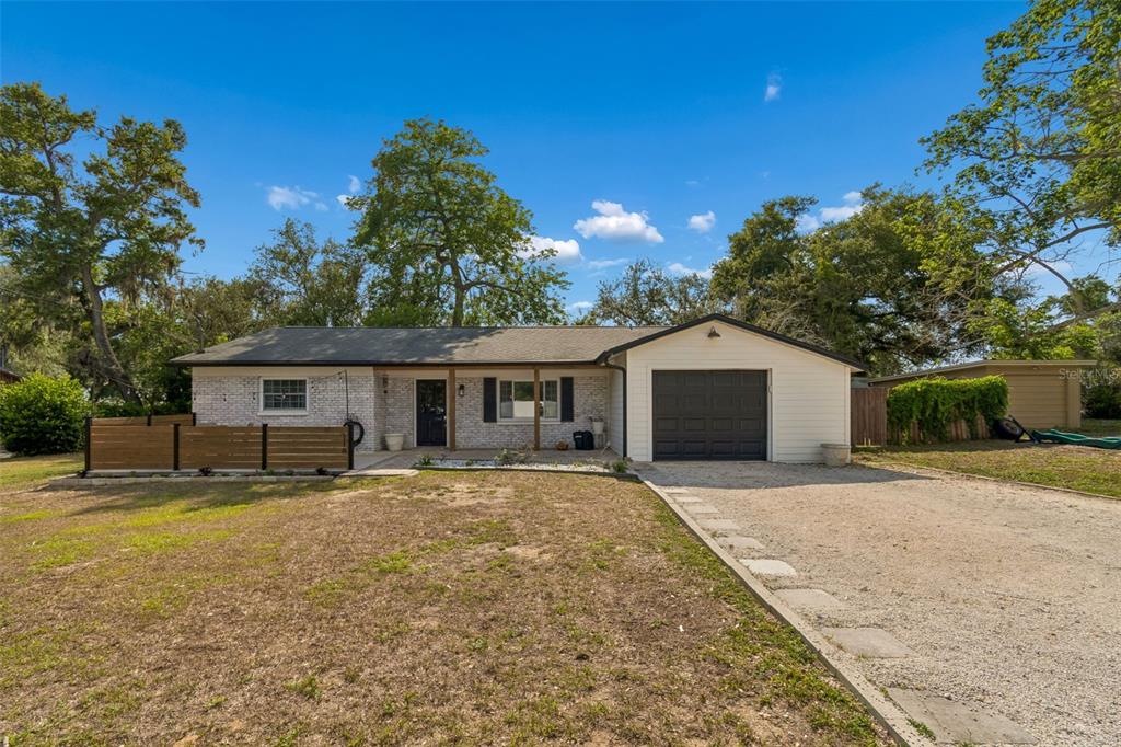 A single-story house with a white brick facade, a dark garage door, and a gravel driveway — 118 HORST ROAD, BRANDON, FL