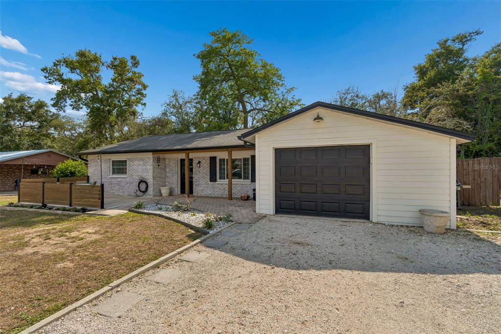 A single-story house with a white brick facade, a black garage door, and a gravel driveway — 118 HORST ROAD, BRANDON, FL