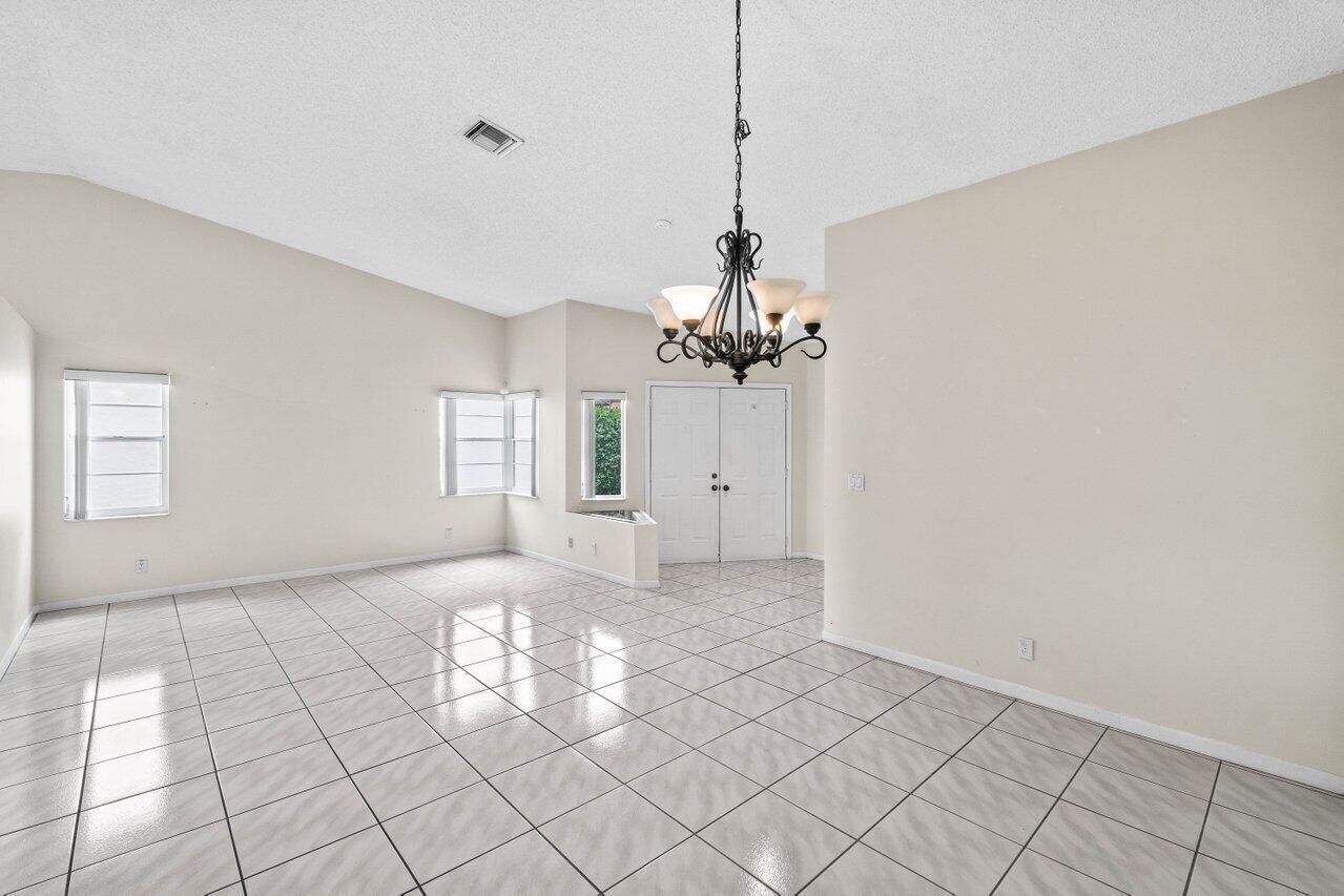 A bright, empty dining room features white tiled floors, a chandelier, and double entry doors — 10001 Country Brook Road, Boca Raton FL 33428, BOCA RATON, FL