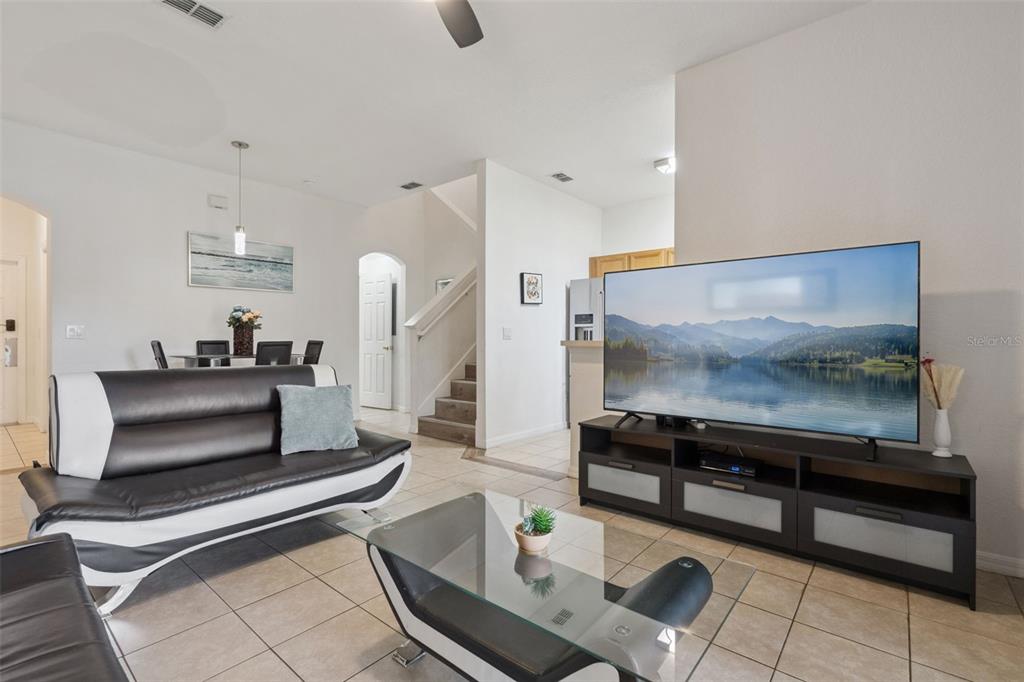 A living room with tile floors, a black and white sofa, and a large television — 245 CAMBRIA AVENUE, DAVENPORT, FL