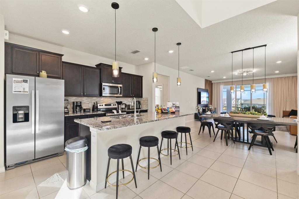 A modern kitchen with dark wood cabinets, granite countertops, and an island with bar stools — 3787 LANA AVENUE, DAVENPORT, FL