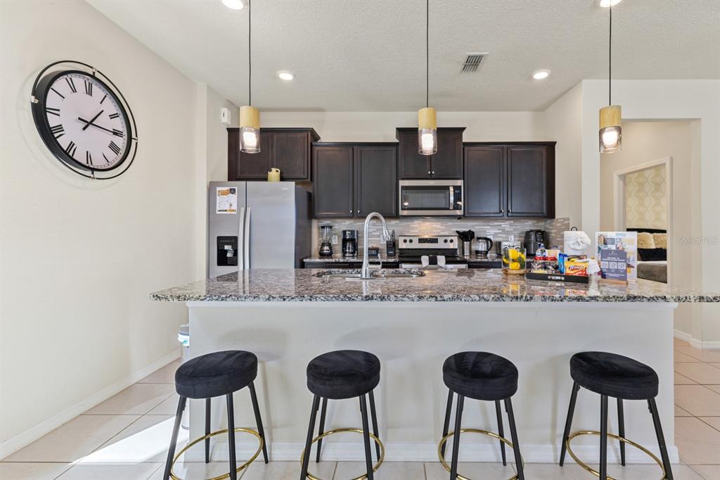 A kitchen features dark wood cabinets, granite countertops, a breakfast bar with four stools, and pendants — 3787 LANA AVENUE, DAVENPORT, FL