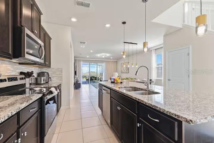 A modern kitchen features dark cabinetry, granite countertops, and a large island with pendant lighting — 3787 LANA AVENUE, DAVENPORT, FL
