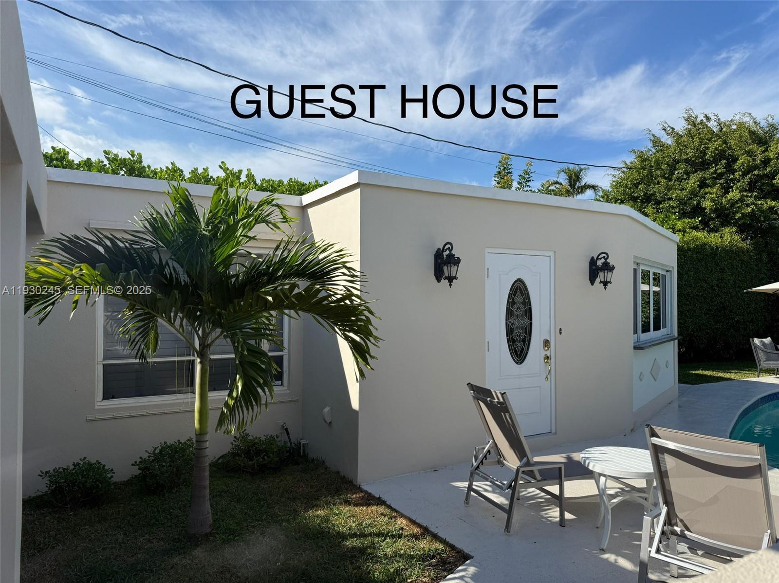 The exterior of a beige guest house features a white door, two wall lamps, and palm trees — 2607 Holy Cross Ln, Lake Worth FL 33460, LAKE WORTH, FL