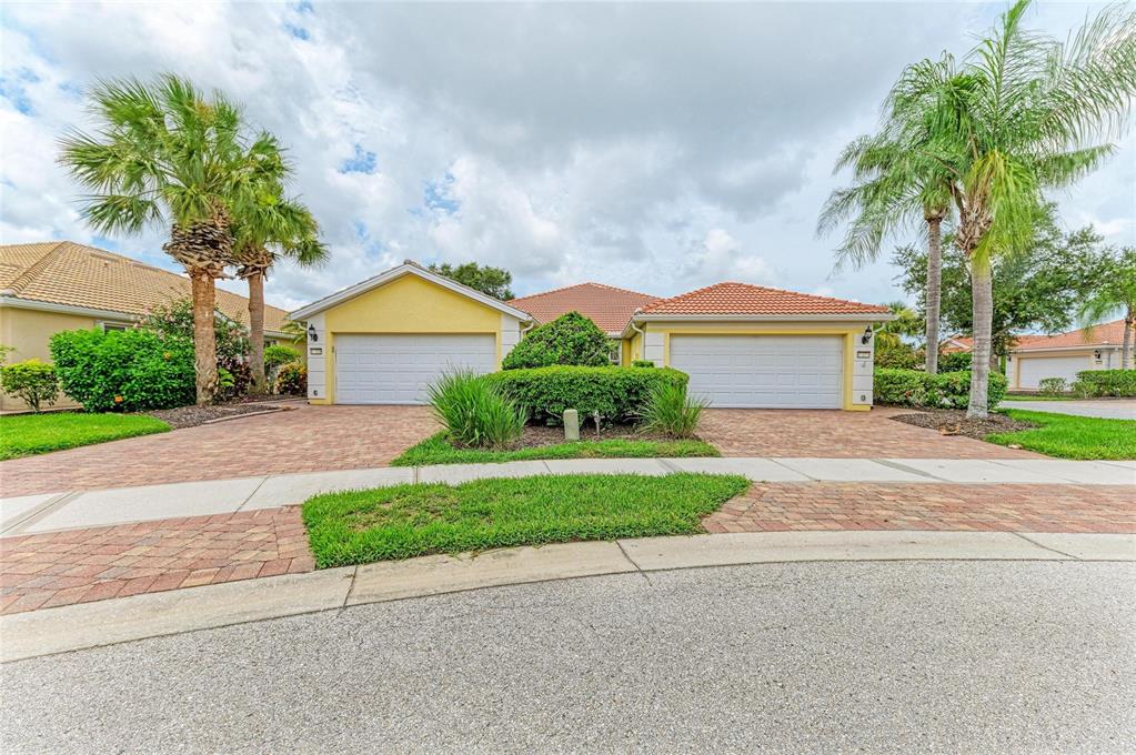 A duplex home with two garage doors, a brick paver driveway, and palm trees — 13275 HUERTA STREET, VENICE, FL