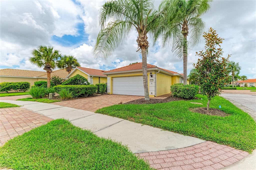 A yellow house with a white garage door and a brick driveway under a cloudy sky — 13275 HUERTA STREET, VENICE, FL