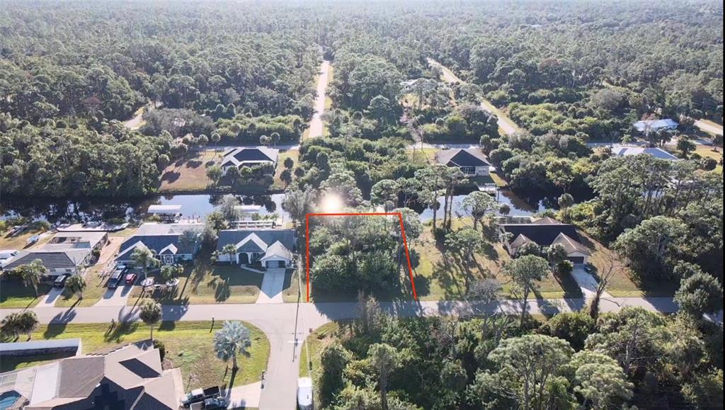 An aerial view shows a vacant, wooded residential lot situated between two houses along a canal — 468 CORY STREET, PORT CHARLOTTE, FL