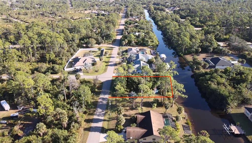An aerial view shows a vacant, tree-covered residential lot situated between a road and a canal — 468 CORY STREET, PORT CHARLOTTE, FL