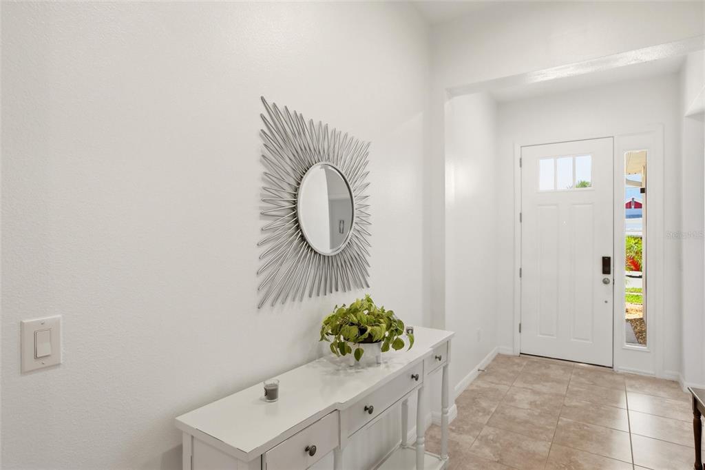 A white entryway features a console table, a sunburst mirror, and a front door — 5720 MAIDENSTONE WAY, PALMETTO, FL