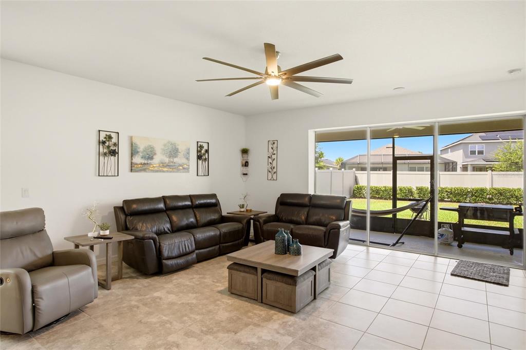 A living room features leather furniture, a coffee table, tile flooring, and sliding glass doors — 5720 MAIDENSTONE WAY, PALMETTO, FL