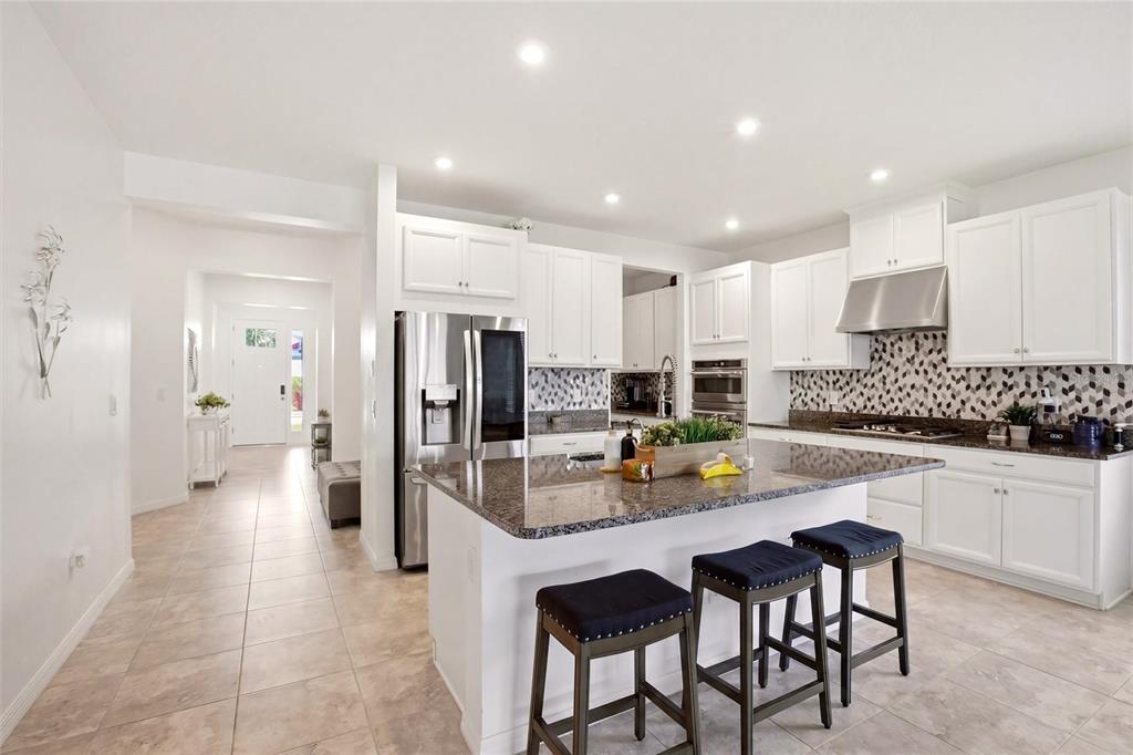 A kitchen features white cabinets, granite countertops, a center island with stools, and tile flooring — 5720 MAIDENSTONE WAY, PALMETTO, FL
