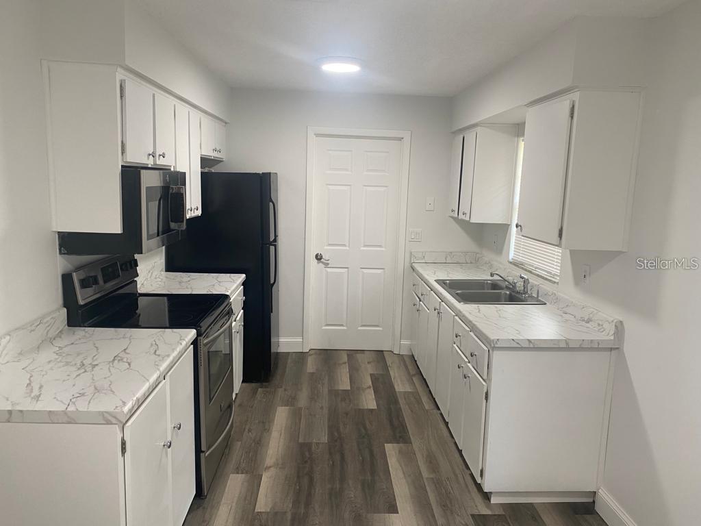 A kitchen features white cabinets, marble-look countertops, stainless steel appliances, and wood-look flooring — 1815 WARFIELD PLACE, SEBRING, FL