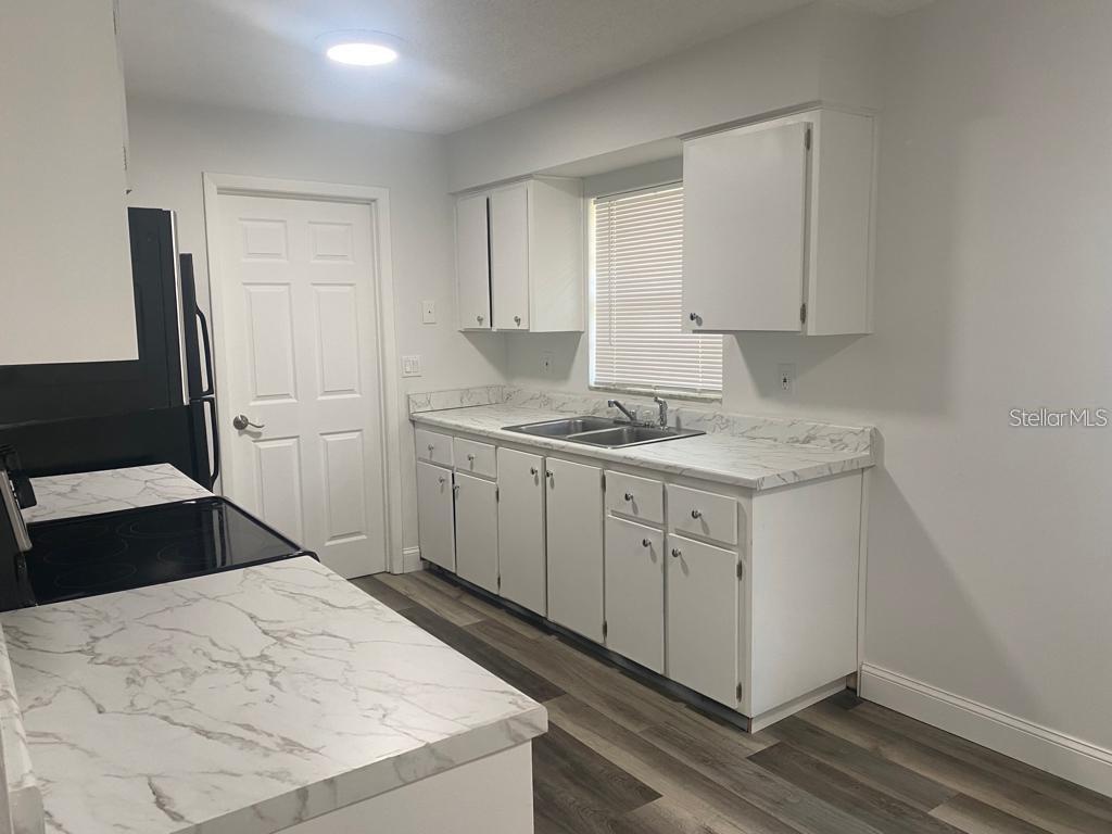 A kitchen features white cabinets, marble-patterned countertops, stainless steel sink, and wood-look flooring — 1815 WARFIELD PLACE, SEBRING, FL