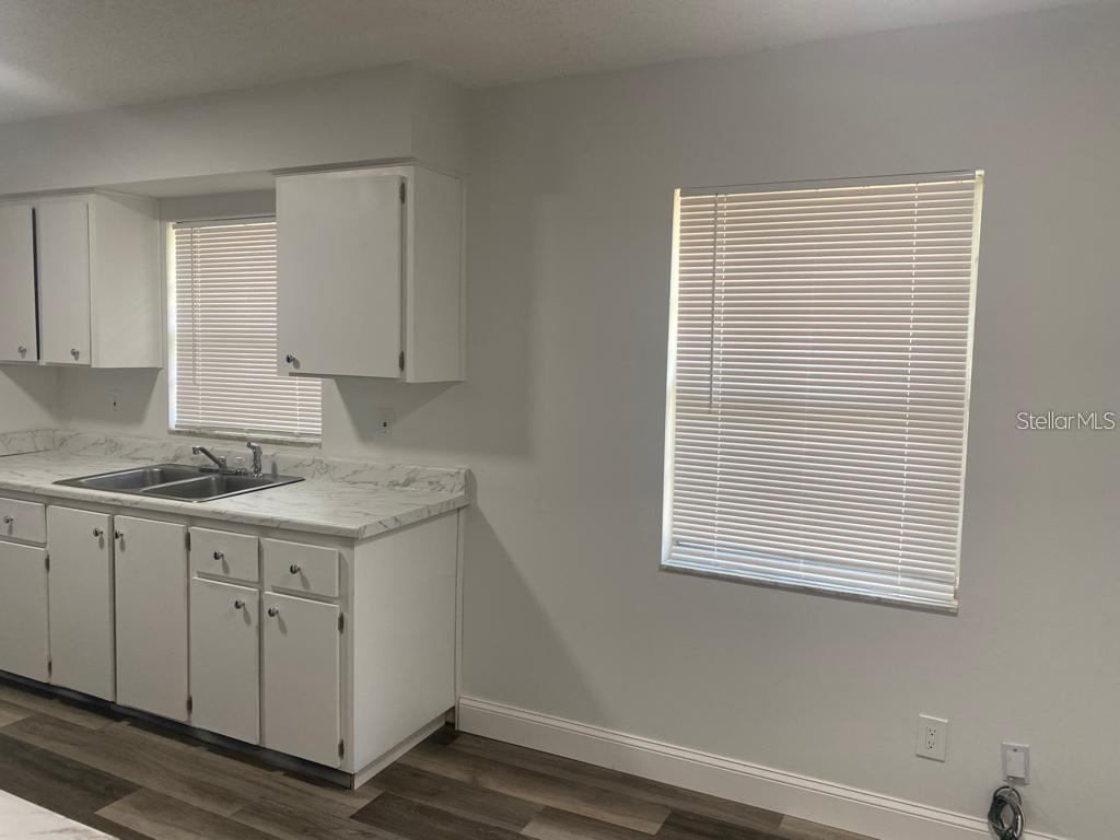 A kitchen features white cabinets, marble-patterned countertops, a stainless steel sink, and two windows — 1815 WARFIELD PLACE, SEBRING, FL