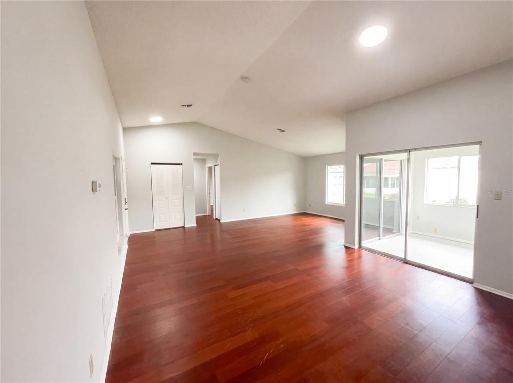An empty living room features hardwood floors, vaulted ceilings, and a sliding glass door — 5508 SILENT BROOK DRIVE, ORLANDO, FL