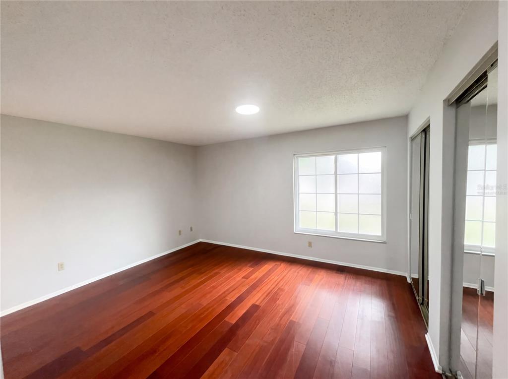 An empty bedroom features light gray walls, dark wood flooring, and a large window — 5508 SILENT BROOK DRIVE, ORLANDO, FL
