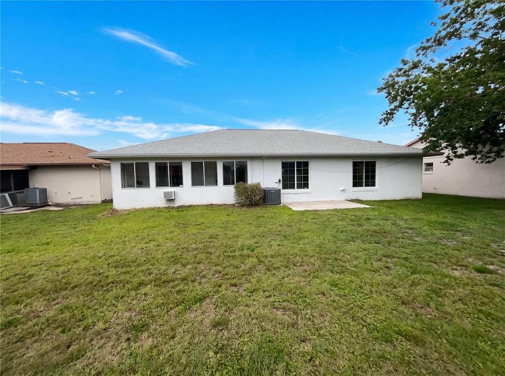 The rear exterior of a single-story house features a white stucco facade and grassy yard — 5508 SILENT BROOK DRIVE, ORLANDO, FL
